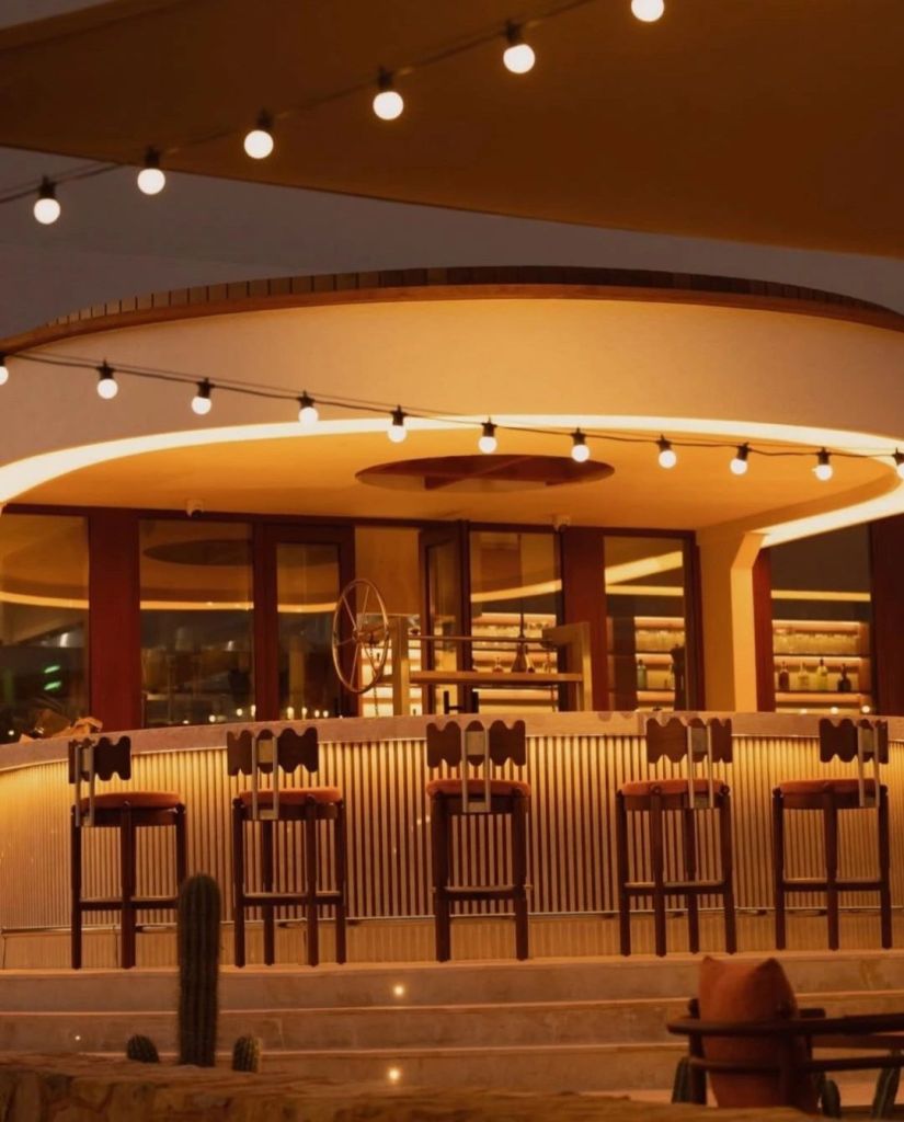 Interior view of a stylish bar area with warm lighting and modern seating, featuring a circular ceiling and decorative string lights.