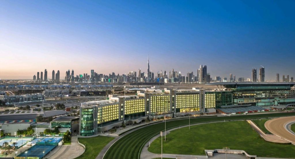 A panoramic view of the Dubai skyline during twilight, featuring the Burj Khalifa, with modern architecture in the foreground, including a horse racing track and facilities.