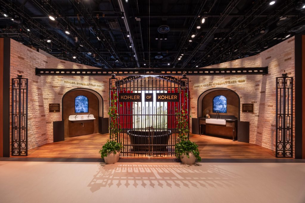 An interior display featuring Kohler products, with stone walls, decorative gates, and various sinks showcased in an exhibition setting.