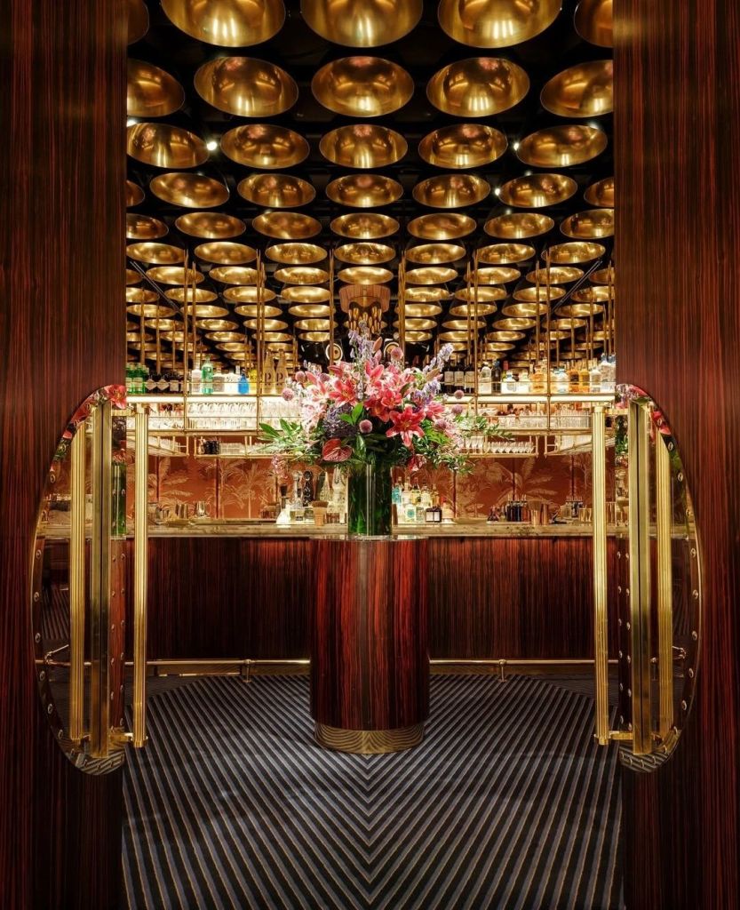 Luxurious bar interior featuring a golden ceiling, vibrant floral arrangement, and elegant decor.