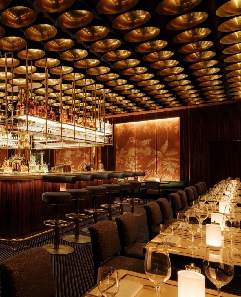 Interior view of a stylish restaurant featuring a bar with a golden ceiling, elegant seating, and ambient lighting.