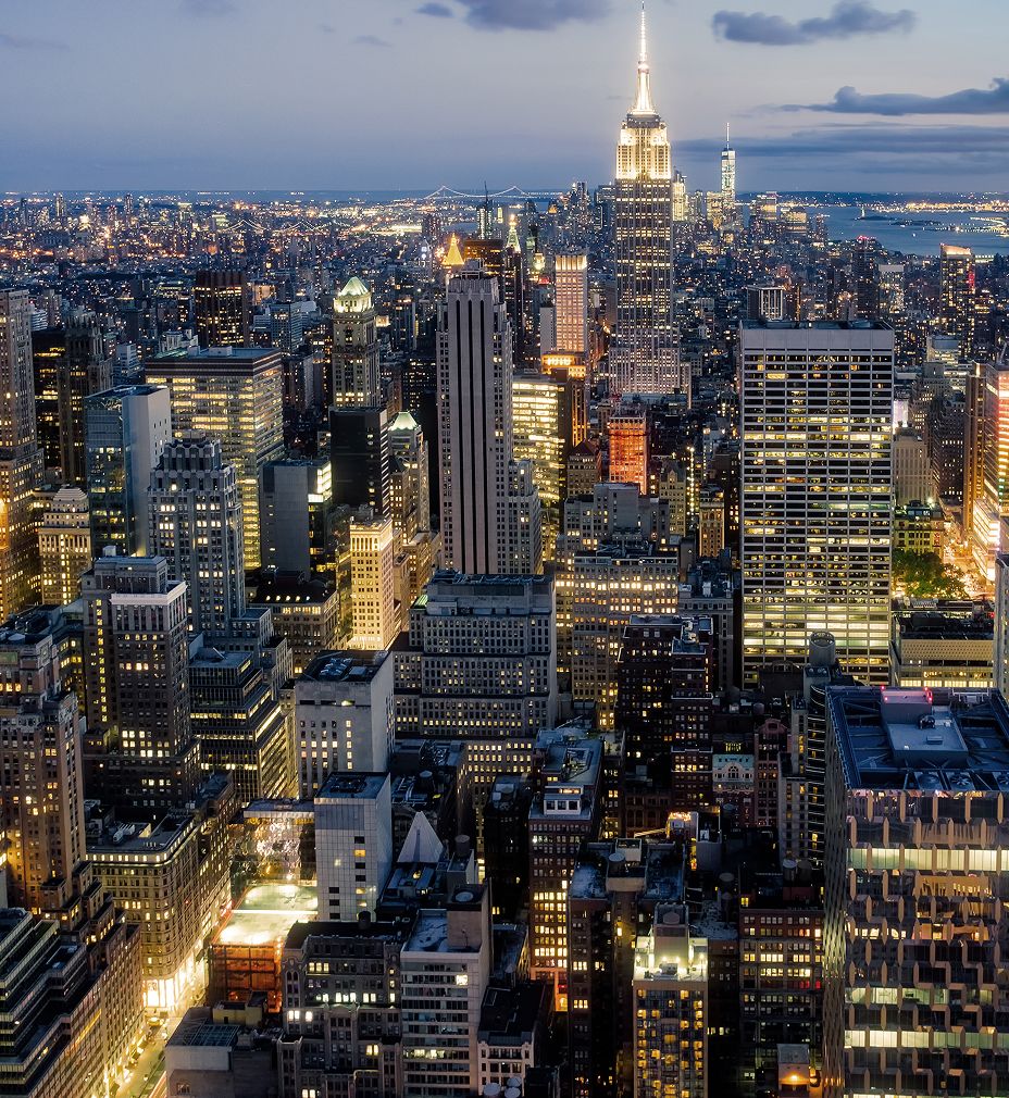 Aerial view of a bustling New York City skyline at twilight, featuring the Empire State Building illuminated against a backdrop of city lights and skyscrapers.