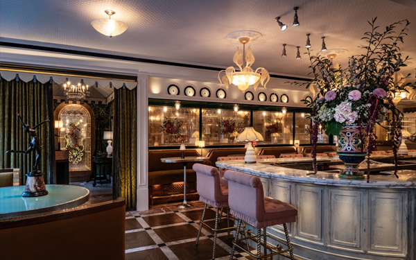 A luxurious restaurant interior featuring a marble bar, plush seating, and elegant floral arrangements under soft lighting.