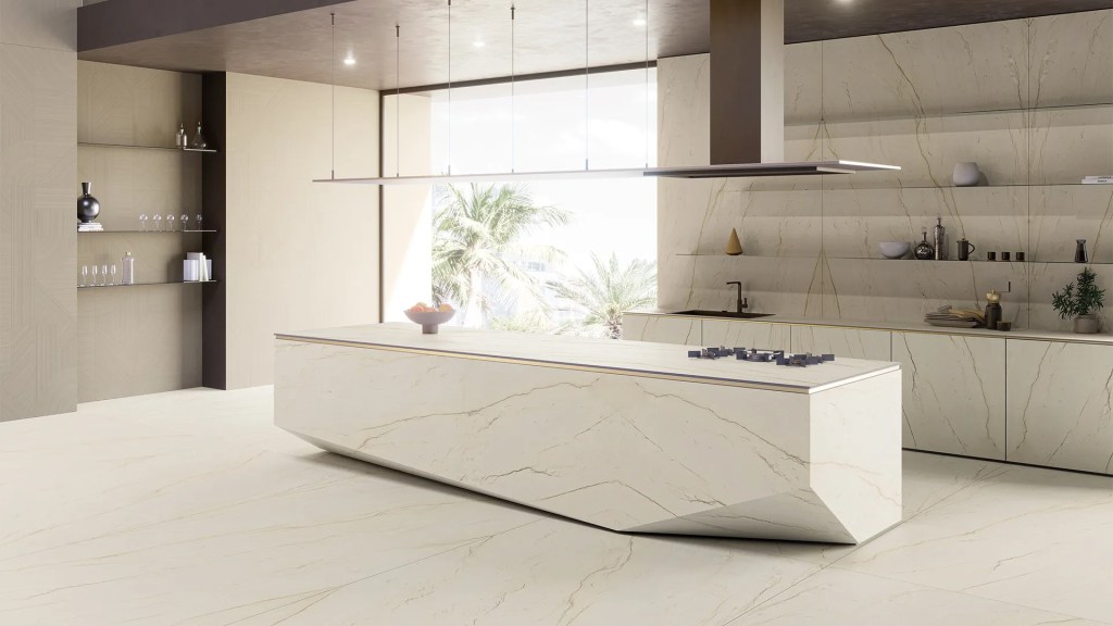 Modern kitchen with a large, angular island featuring a gas hob, surrounded by minimalistic cabinetry and a backdrop of palm trees visible through the window.