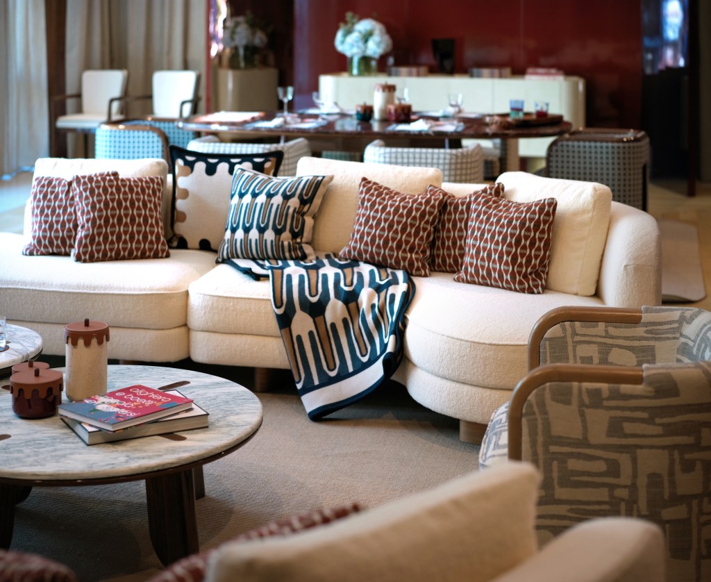 A stylish living room featuring a curved sofa adorned with patterned cushions and a decorative throw, complemented by a marble coffee table with various decorative items.