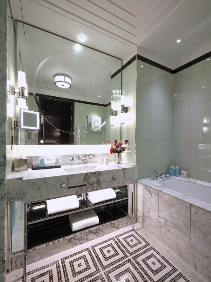 Luxurious bathroom featuring a marble vanity with a large round mirror, a bathtub, and decorative tiles.