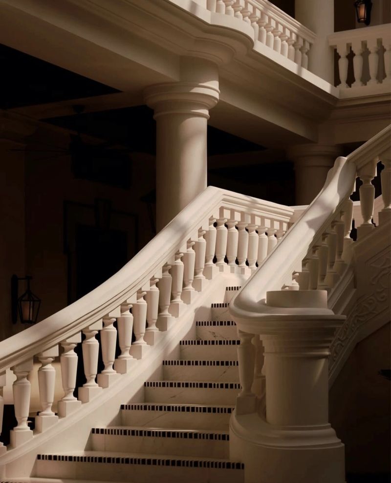 Elegant curved staircase with intricate balustrades and shadowed lighting, showcasing a blend of architectural beauty and classic design.