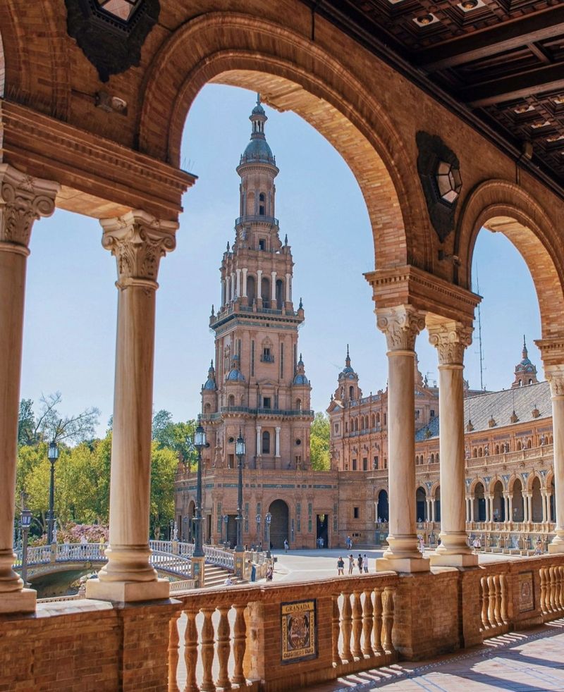 View of a grand tower through arched columns, surrounded by historic buildings and greenery.