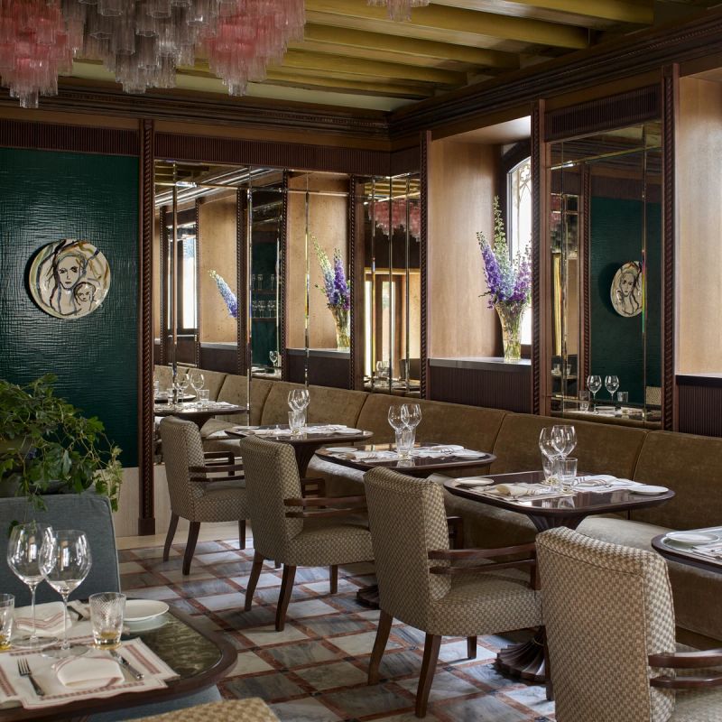 Elegant restaurant interior featuring a blend of dark wood and green accents, with plush seating, glassware on tables, and decorative floral arrangements.