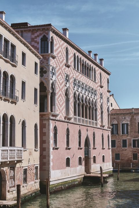 A historic pink and white patterned building along a canal in Venice, showcasing intricate architecture and arched windows.